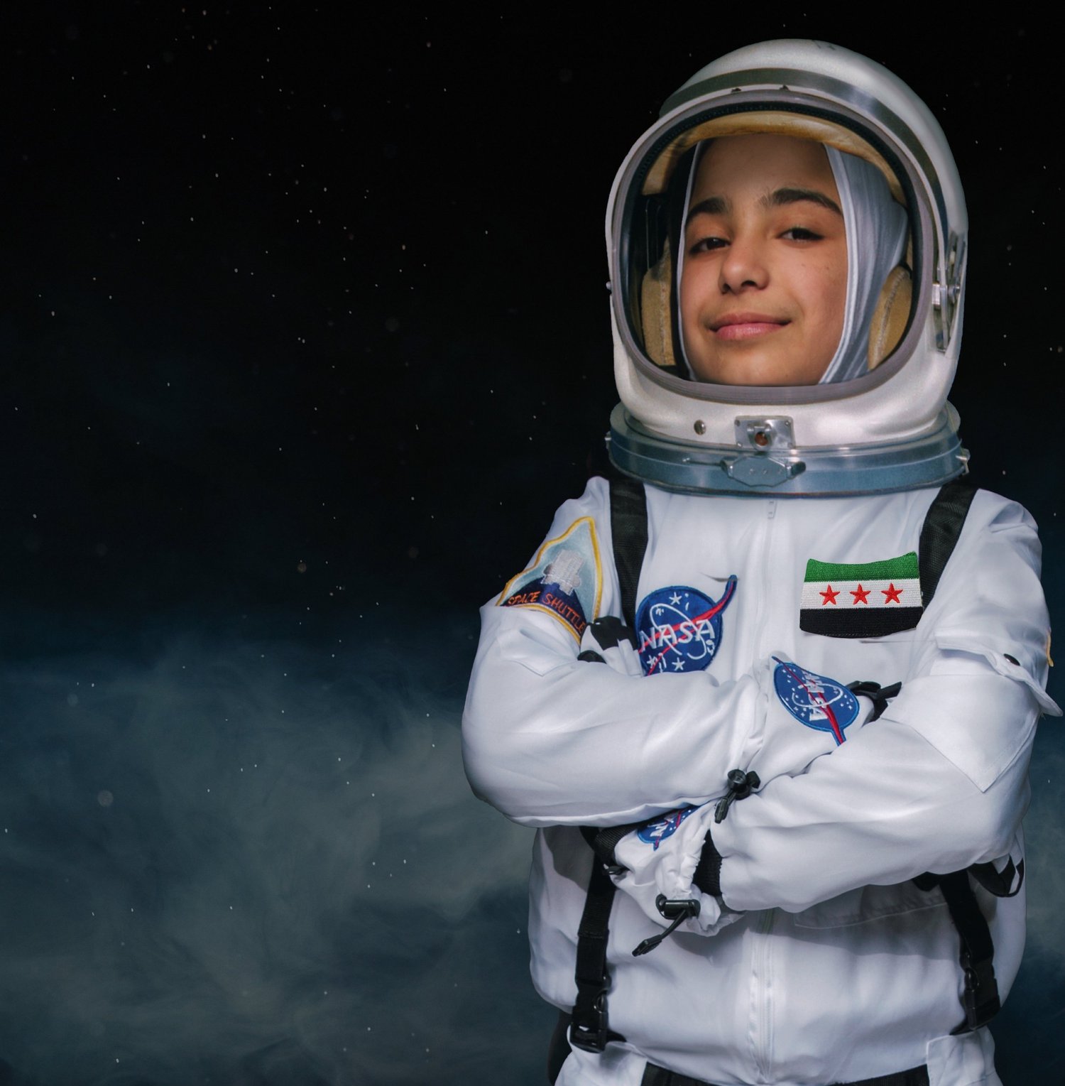 A young girl portrayed as an astronaut in a spacesuit with a Syrian flag patch against a starfield.