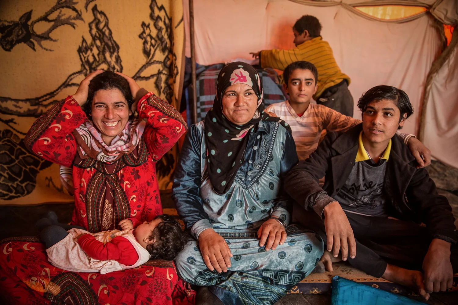 Family seated together on patterned blankets inside a tent shelter